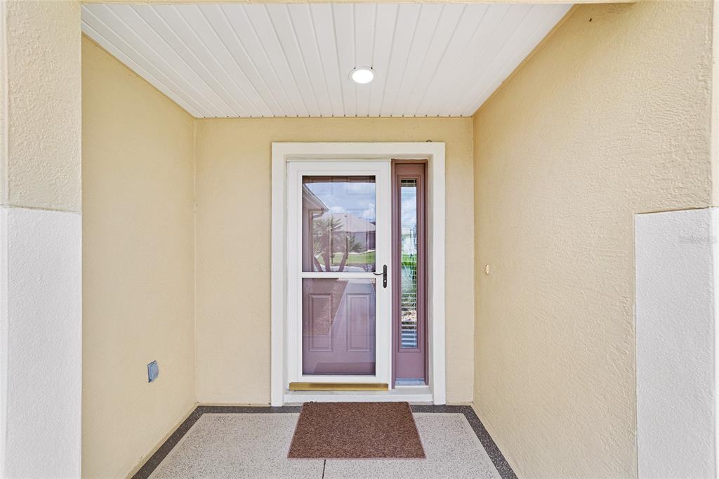A covered entryway features a front door with a storm door and a side window — 8588 SE 134TH STREET, SUMMERFIELD, FL