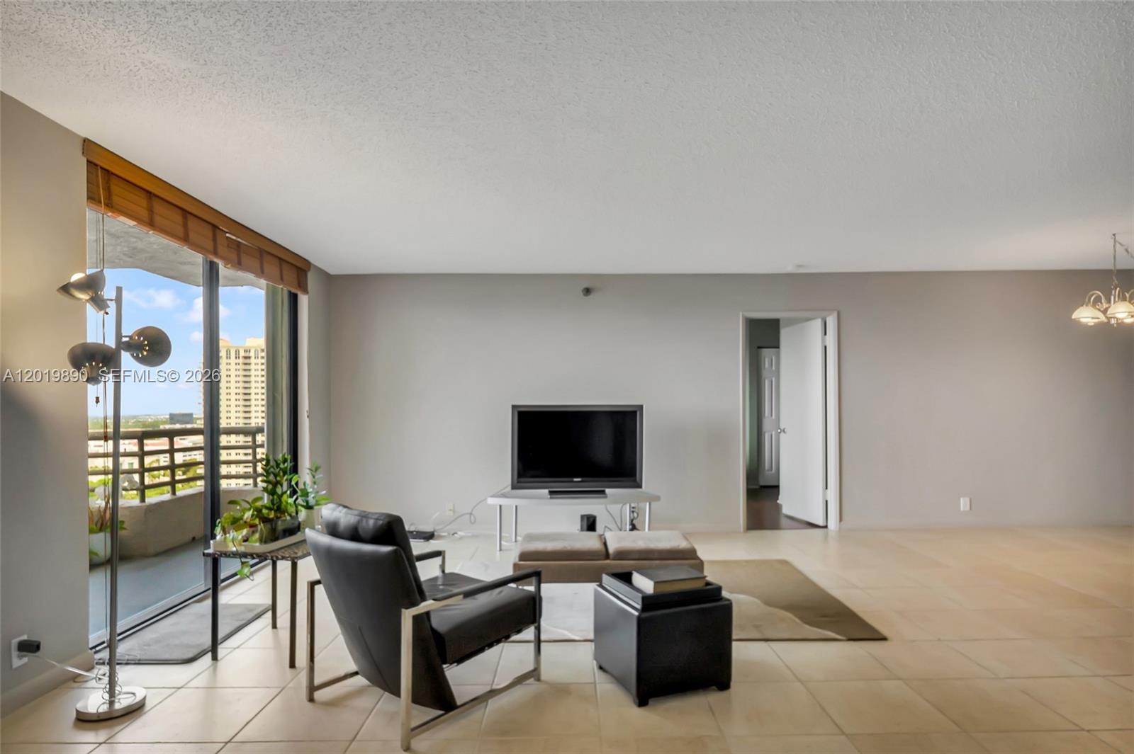 A living room features tile flooring, a television on a stand, and a balcony view — 3300 NE 191st St, Aventura FL 33180, AVENTURA, FL