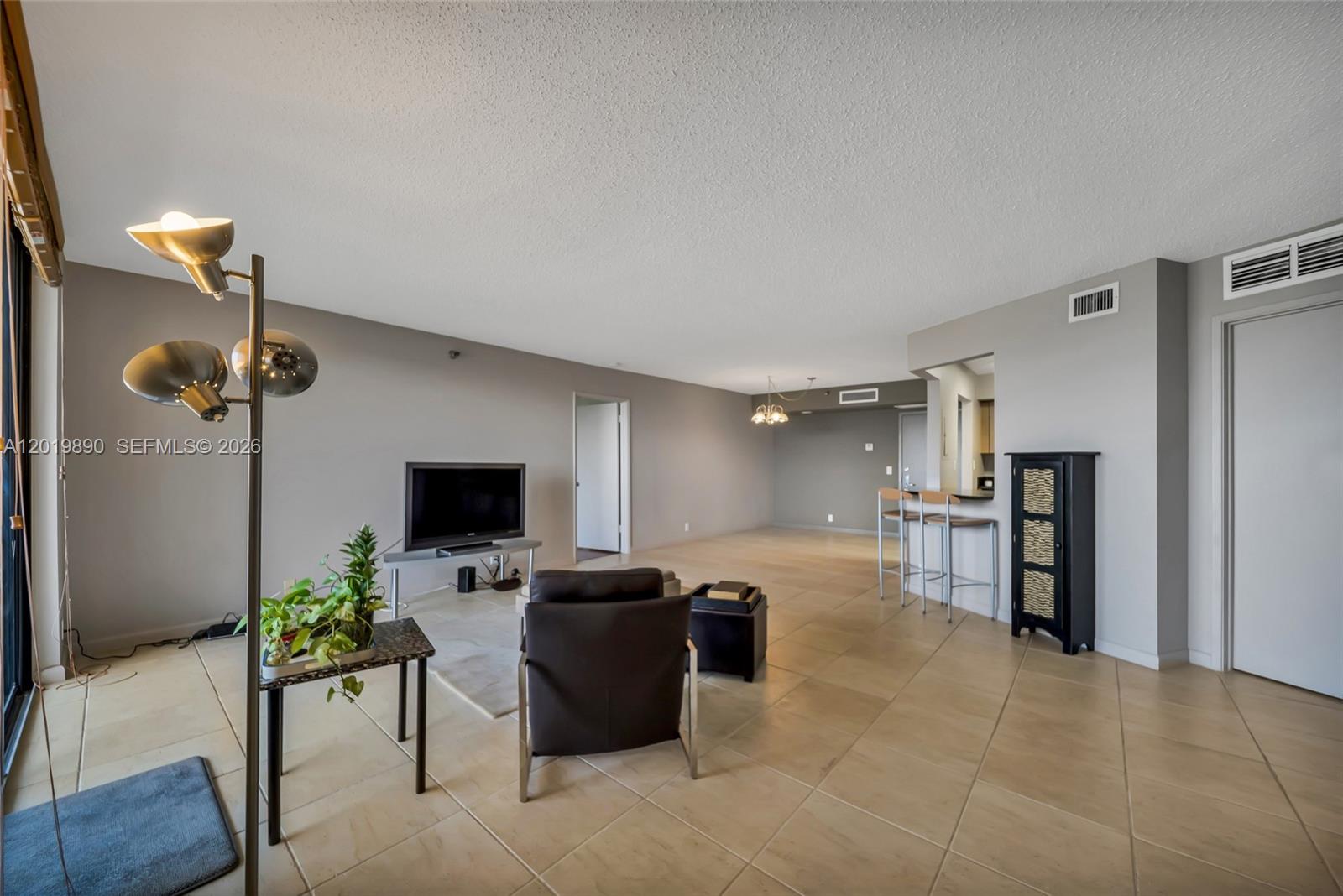 A living room features tile flooring, a television, a leather chair, and a breakfast bar — 3300 NE 191st St, Aventura FL 33180, AVENTURA, FL