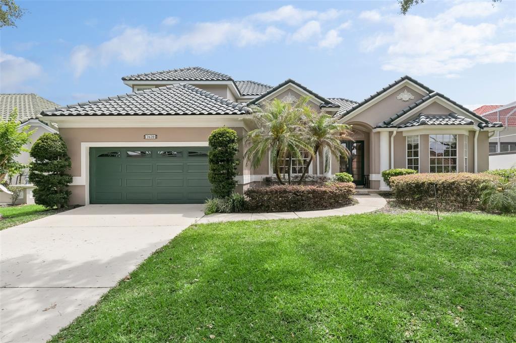 A single-story house with a green garage door, tile roof, and a front lawn — 7670 MILANO DRIVE, ORLANDO, FL