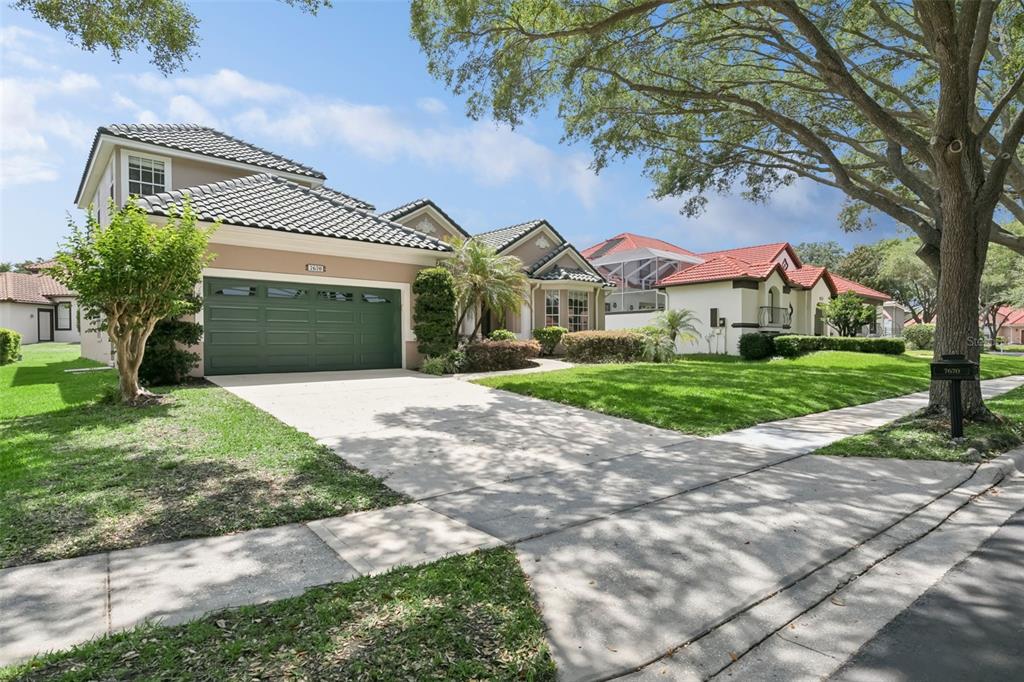 A two-story house with a green garage door and a tiled roof sits on a lawn — 7670 MILANO DRIVE, ORLANDO, FL