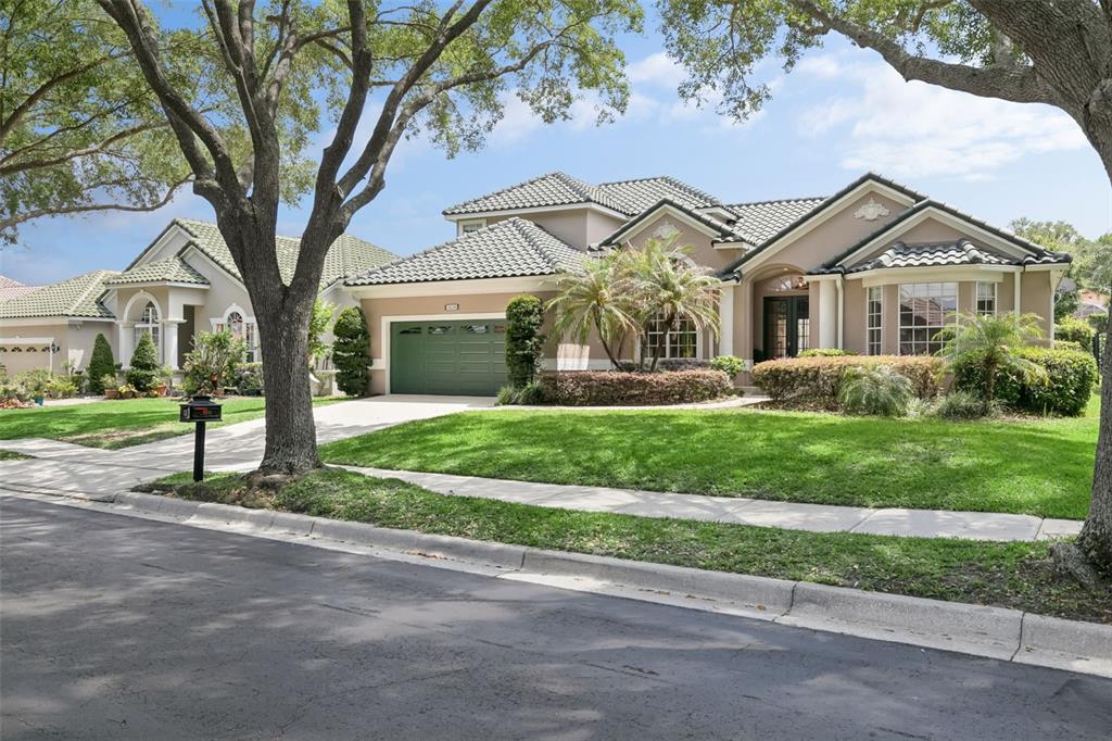 A single-story suburban house with a green garage door, tile roof, and landscaped front yard — 7670 MILANO DRIVE, ORLANDO, FL