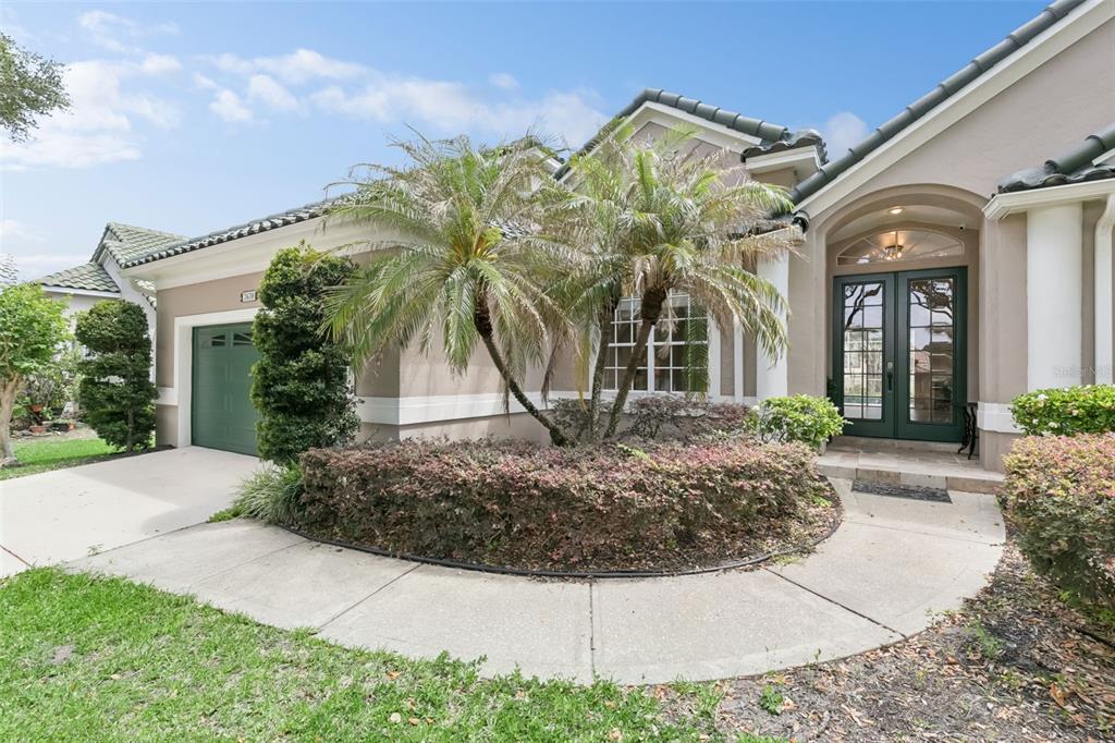 A single-story house with a green garage door, double front doors, and a palm tree garden — 7670 MILANO DRIVE, ORLANDO, FL