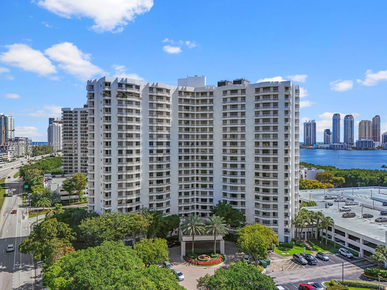 An aerial view of a tall white residential building with balconies and surrounding parking lots — 3300 NE 192nd St # 603, Aventura FL 33180, AVENTURA, FL