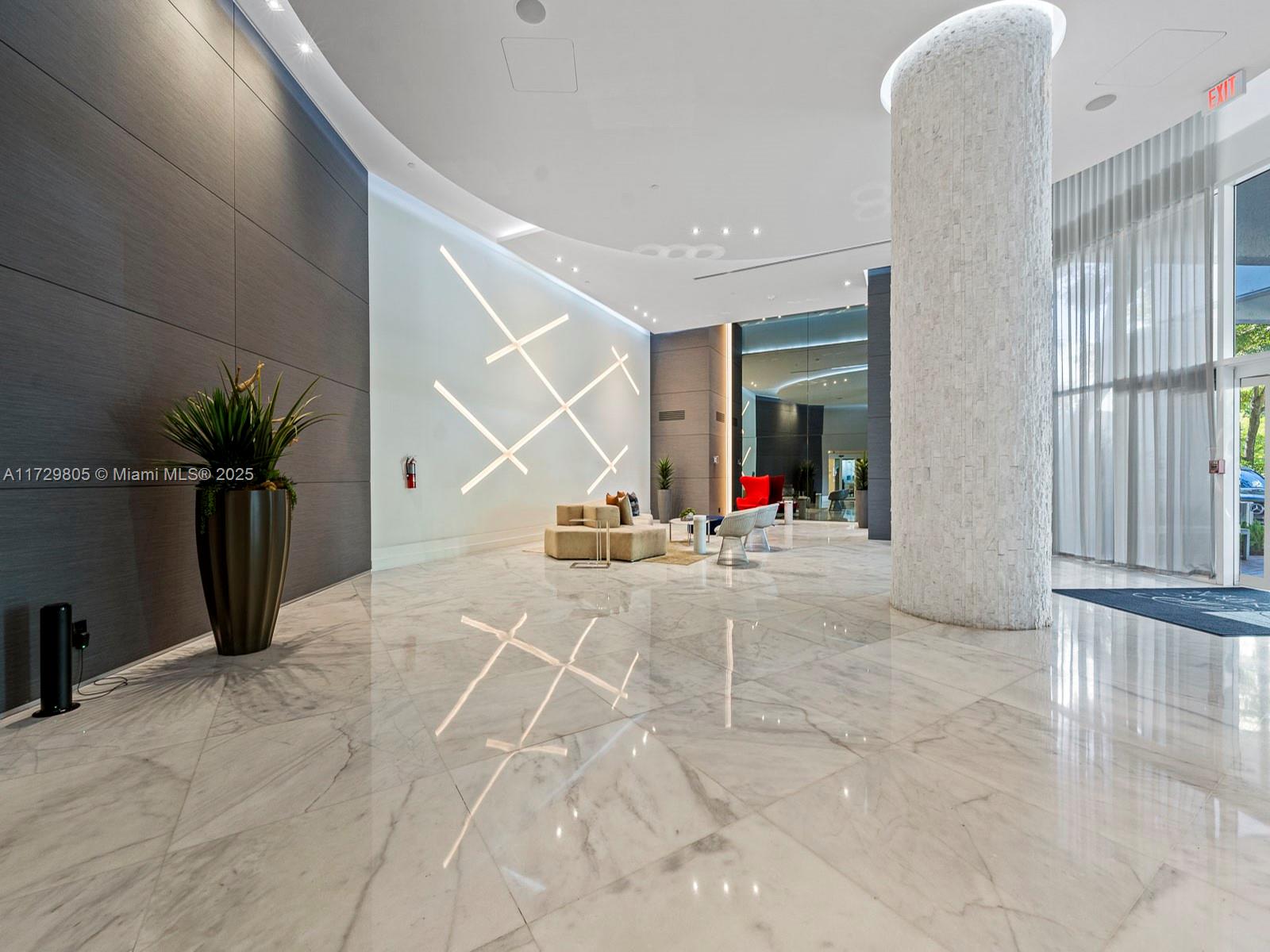 A modern building lobby features a large stone pillar, marble floors, and geometric wall lighting — 3300 NE 192nd St # 603, Aventura FL 33180, AVENTURA, FL