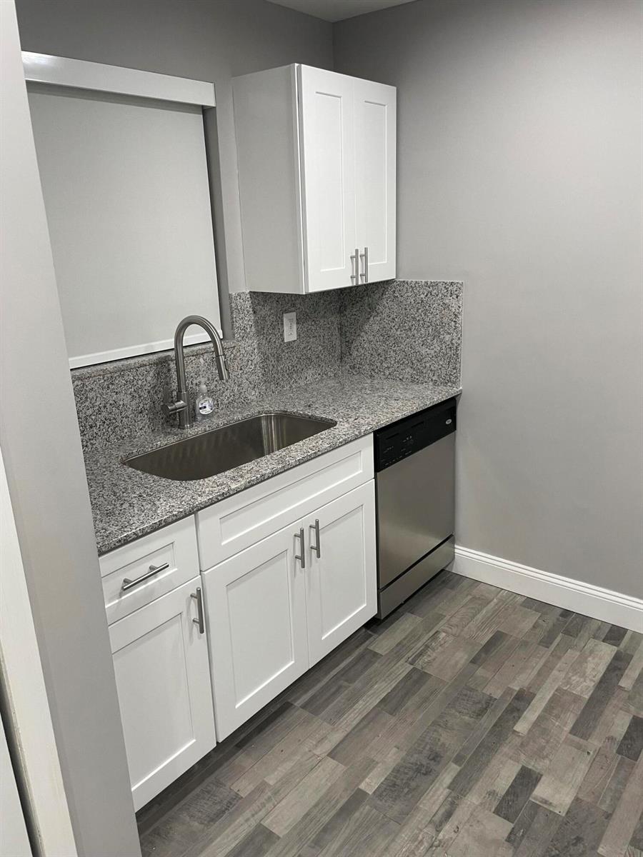 A kitchen area features white cabinets, granite countertops, a stainless steel sink, and a dishwasher — 2700 Coral Springs Drive # 104, Coral Springs FL 33065, CORAL SPRINGS, FL