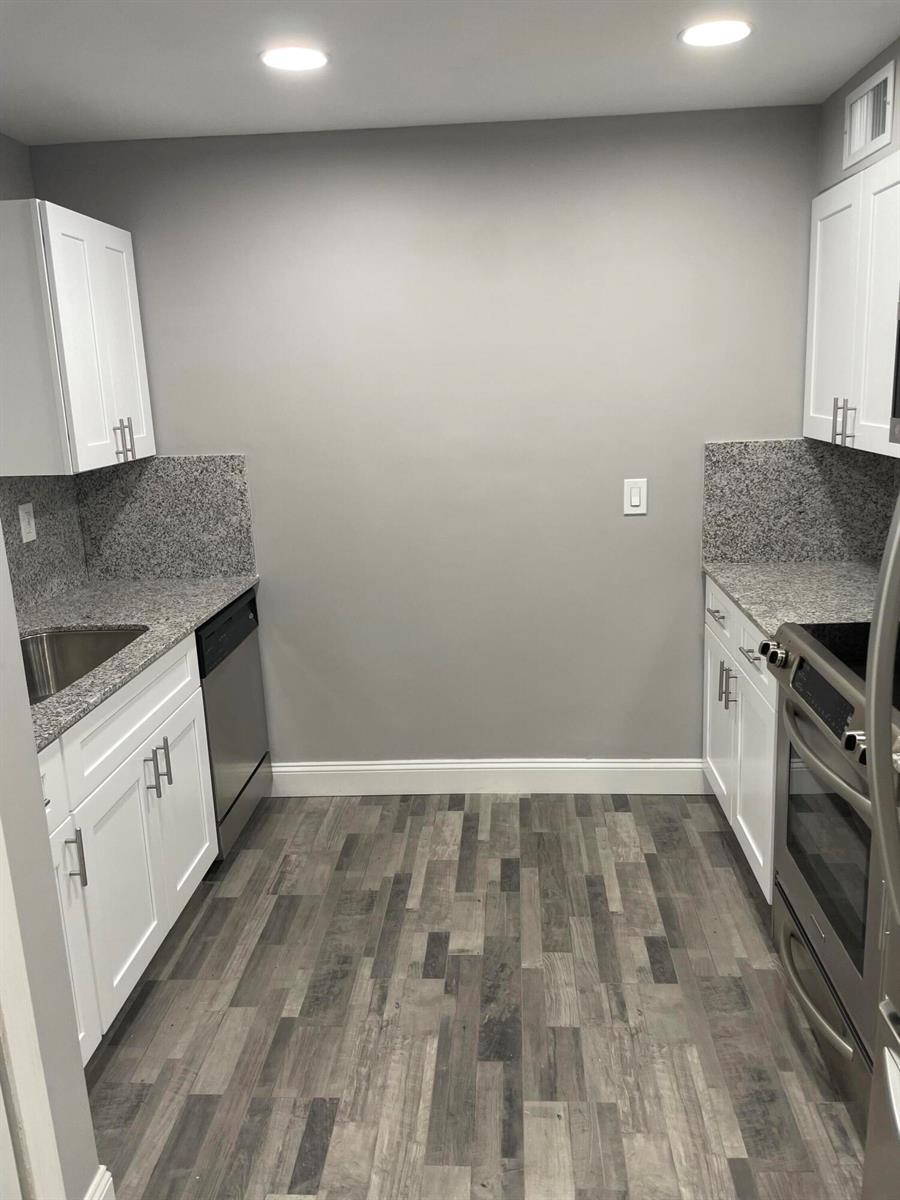 A galley kitchen features white cabinets, granite countertops, stainless steel appliances, and wood-look flooring — 2700 Coral Springs Drive # 104, Coral Springs FL 33065, CORAL SPRINGS, FL