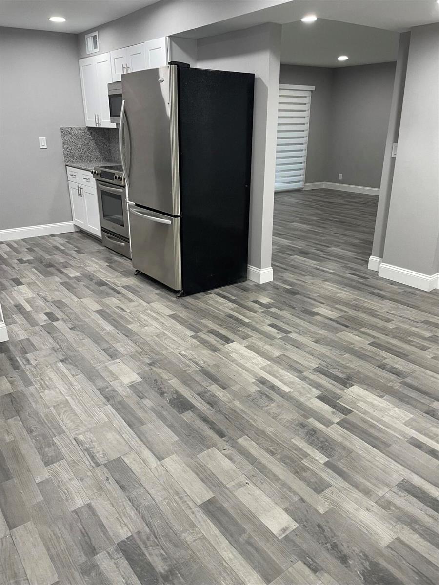 A kitchen with stainless steel appliances and white cabinets opens into a gray-walled living area — 2700 Coral Springs Drive # 104, Coral Springs FL 33065, CORAL SPRINGS, FL