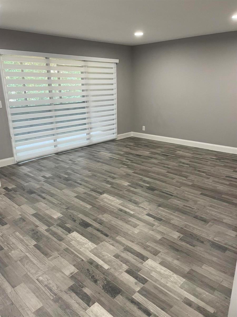 An empty room features gray walls, wood-look laminate flooring, and a sliding glass door — 2700 Coral Springs Drive # 104, Coral Springs FL 33065, CORAL SPRINGS, FL