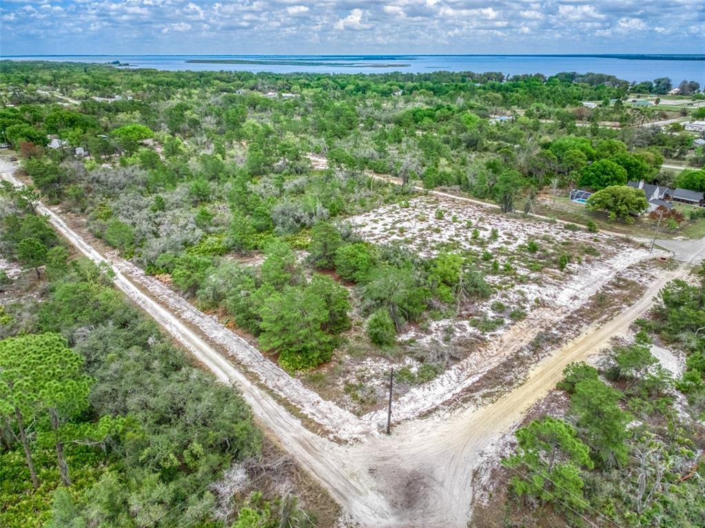 An aerial view shows a vacant, sandy, wooded lot bordered by dirt roads near water — 143 PATTON AVENUE, LAKE PLACID, FL