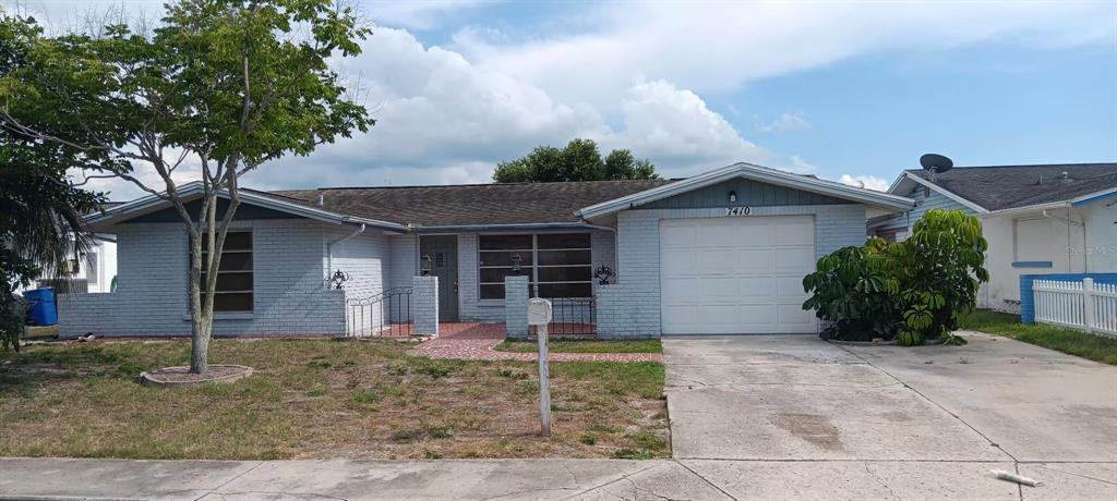 A single-story light blue brick house features a front-facing garage and a paved walkway — 7410 MORAVIAN DRIVE, PORT RICHEY, FL