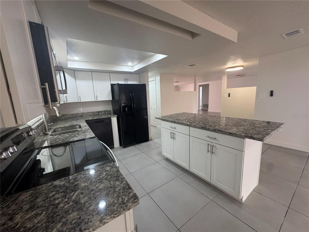 A kitchen features white cabinets, granite countertops, a black refrigerator, and gray tile flooring — 7410 MORAVIAN DRIVE, PORT RICHEY, FL