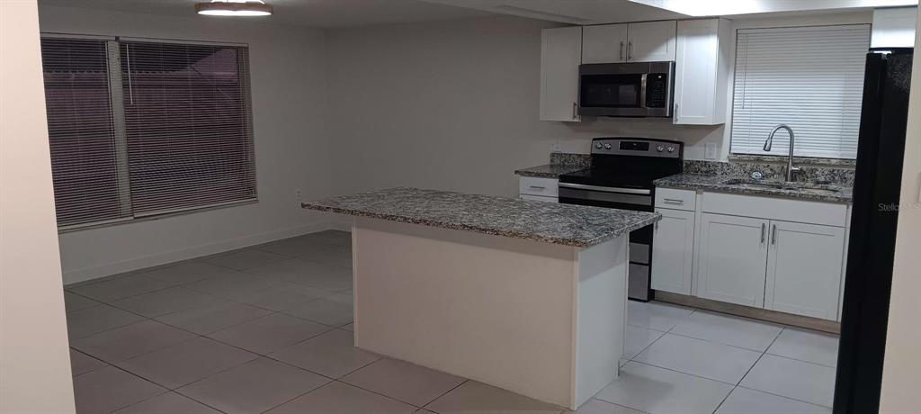 A kitchen with white cabinets, granite countertops, a center island, and light-colored tile flooring — 7410 MORAVIAN DRIVE, PORT RICHEY, FL