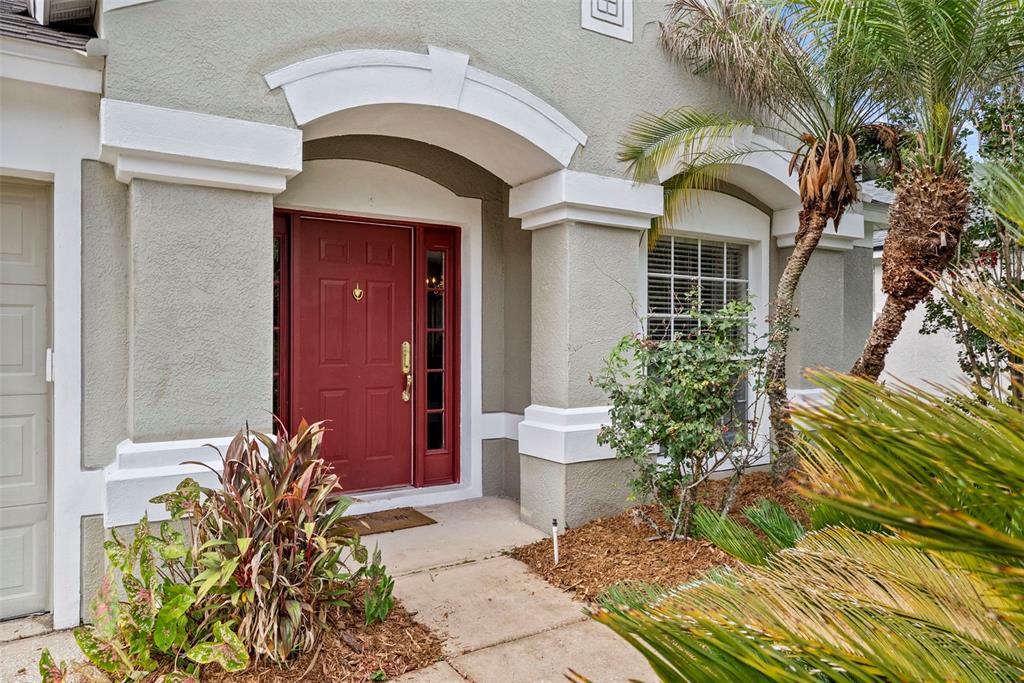 A red front door is framed by white architectural arches and columns on a house exterior — 5868 WAR ADMIRAL DRIVE, WESLEY CHAPEL, FL