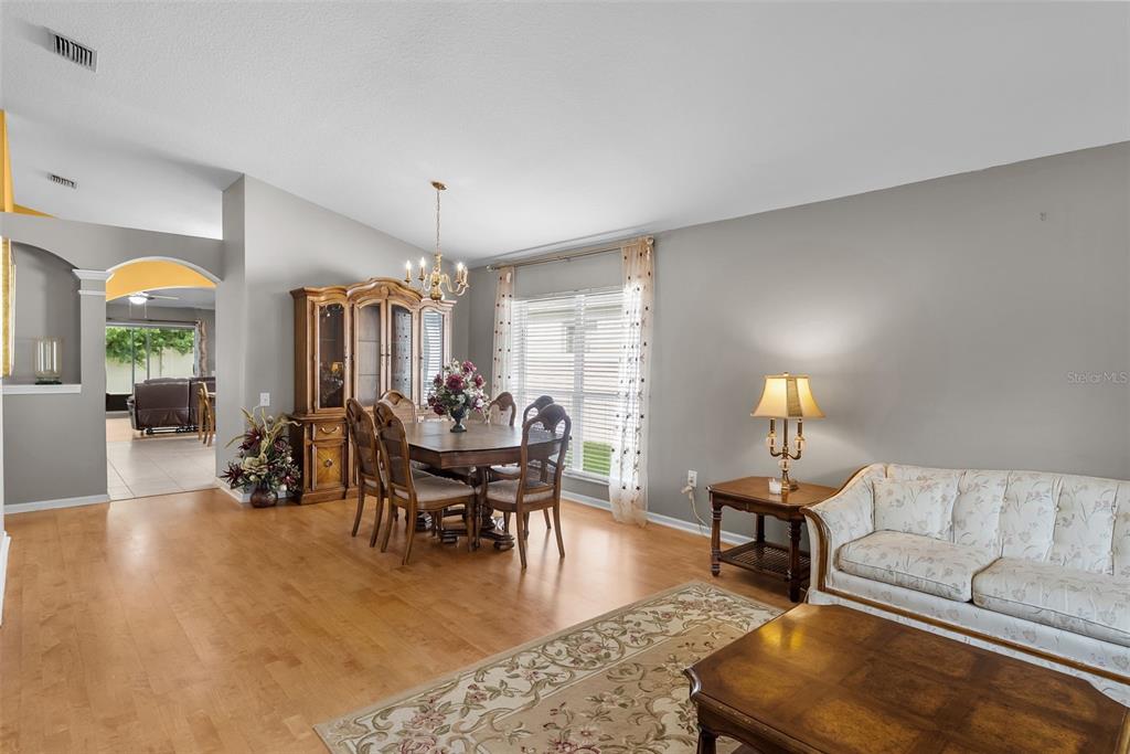 A dining area and living room feature hardwood floors, a wooden hutch, and a floral sofa — 5868 WAR ADMIRAL DRIVE, WESLEY CHAPEL, FL