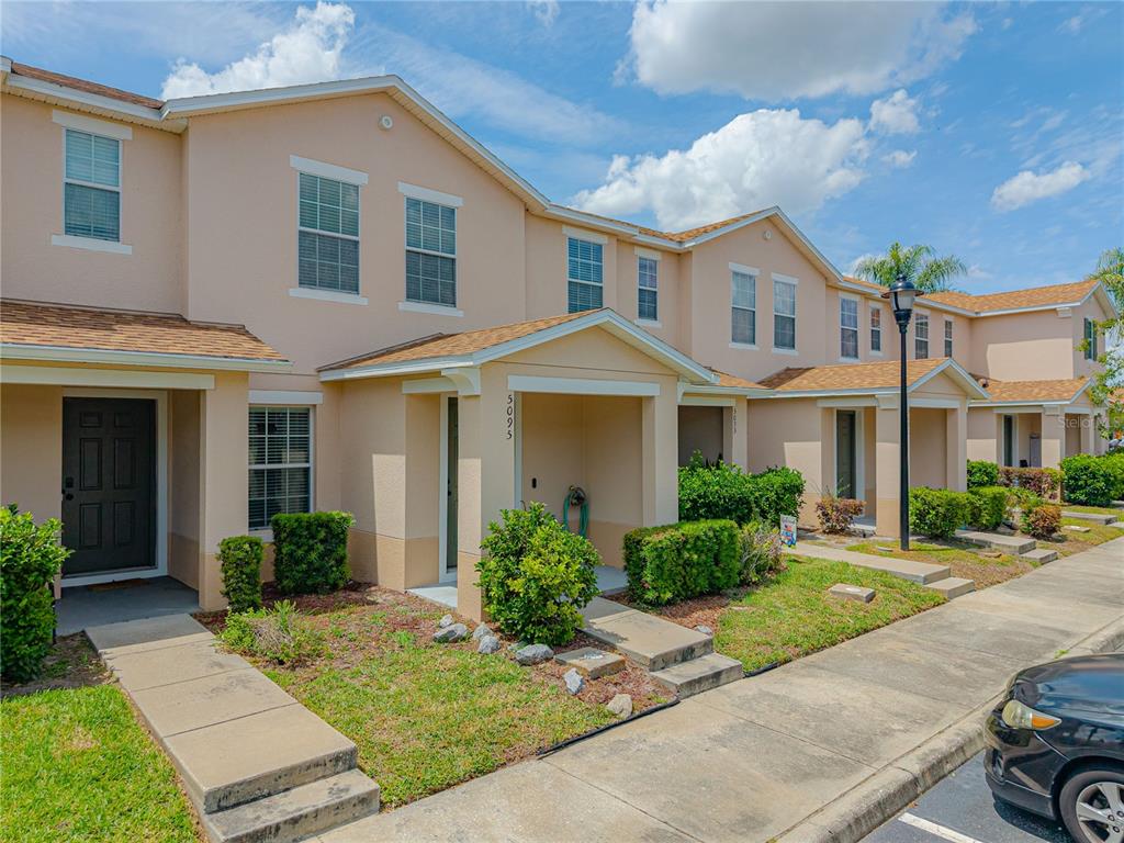 A row of tan two-story townhomes with shingled roofs and small front porches — 5095 DOMINICA DRIVE, KISSIMMEE, FL