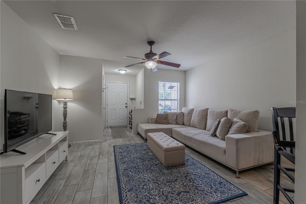 A living room features a sectional sofa, a blue patterned rug, and light wood-look flooring — 5095 DOMINICA DRIVE, KISSIMMEE, FL