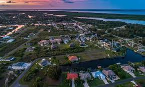 An aerial view shows a residential neighborhood with houses situated along a canal at sunset — 10425 WINNIPEG STREET, PORT CHARLOTTE, FL