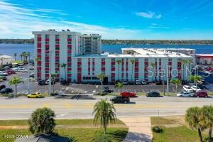 An aerial view shows a multi-story apartment complex with red accents situated near a body of water — 2711 N HALIFAX AVENUE UNIT 370, DAYTONA BEACH, FL