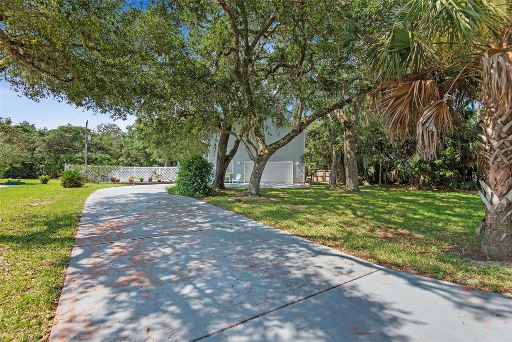 A paved driveway leads toward a garage surrounded by large trees and a grassy yard — 26 BEACHSIDE DRIVE, PALM COAST, FL