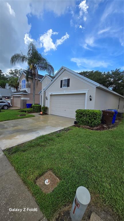 A beige single-story house with a two-car garage, a palm tree, and a green lawn — 1604 EAGLE FEATHER DRIVE, KISSIMMEE, FL