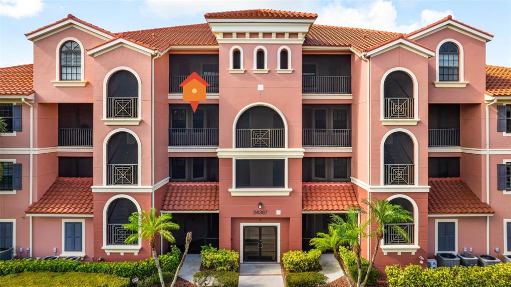 An exterior view of a multi-story pink stucco apartment building with arched balconies and windows — 24367 BALTIC AVENUE UNIT 202, PUNTA GORDA, FL