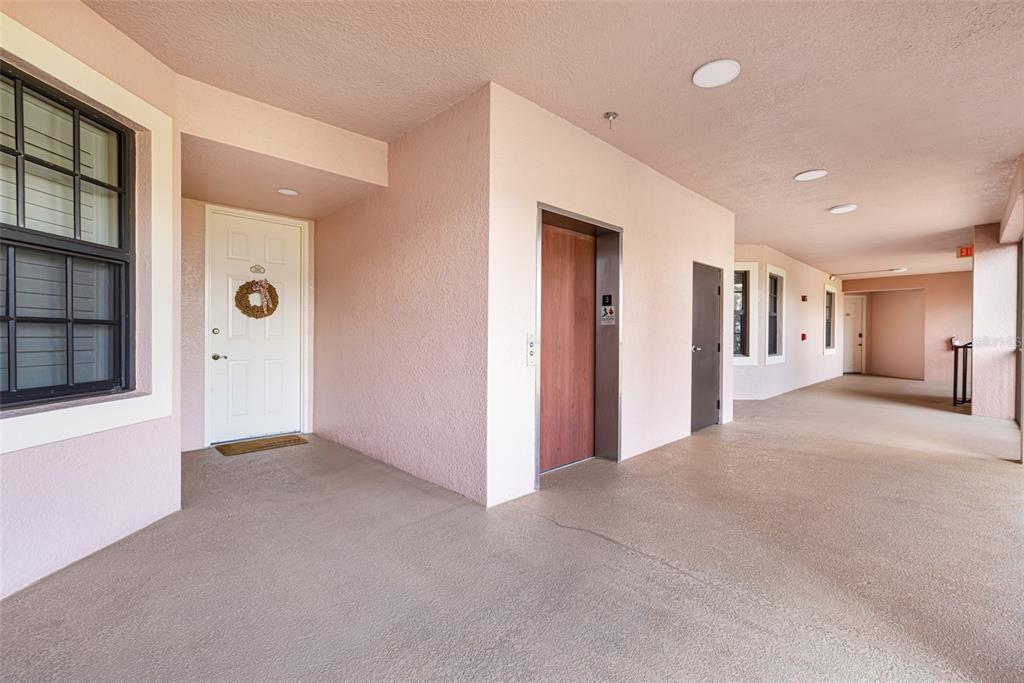 An outdoor apartment hallway features a white front door, an elevator, and beige flooring — 24367 BALTIC AVENUE UNIT 202, PUNTA GORDA, FL