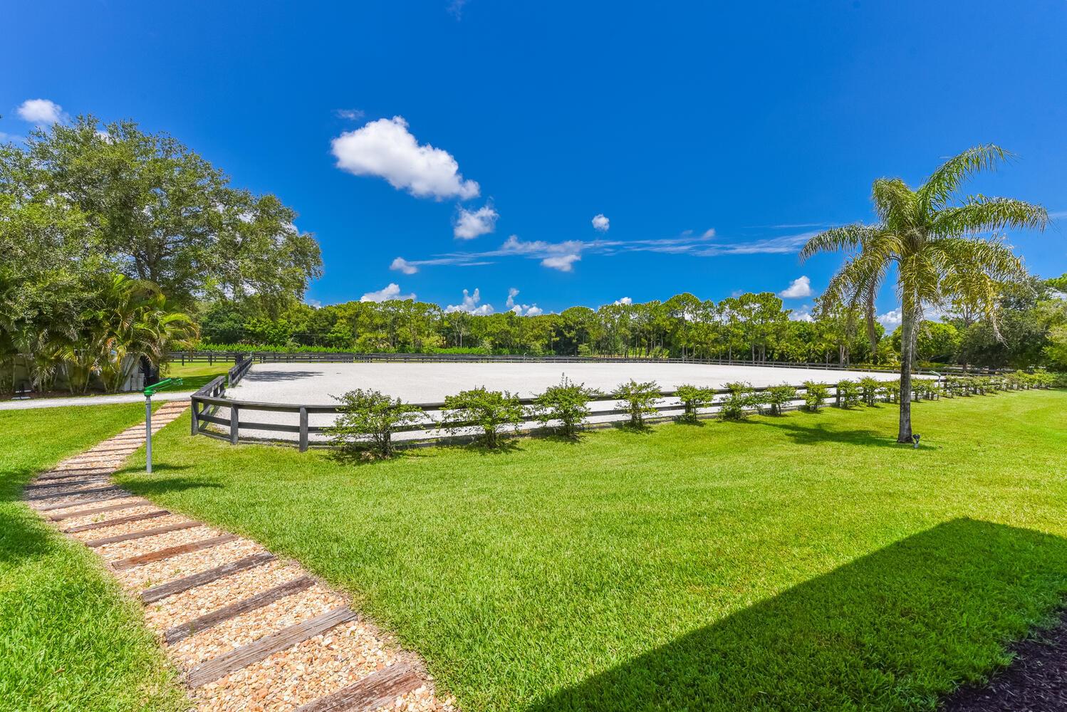 A fenced equestrian riding arena sits in a grassy yard with a stone pathway — 2780 Skipiks Way, Wellington FL 33470, WELLINGTON, FL