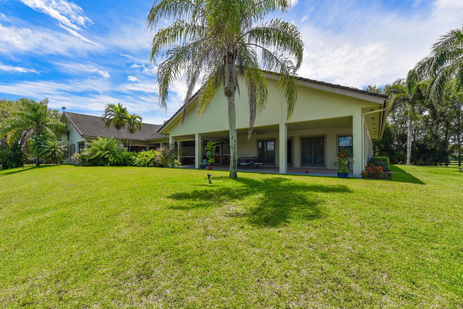 A large, light-colored house with a covered patio, palm trees, and a spacious green lawn — 2780 Skipiks Way, Wellington FL 33470, WELLINGTON, FL