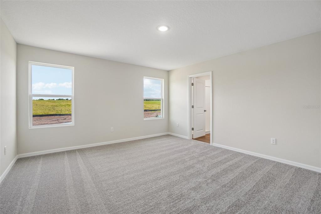An empty bedroom with gray carpet, neutral walls, two windows, and a doorway — 36564 SAGEMOOR DRIVE, ZEPHYRHILLS, FL