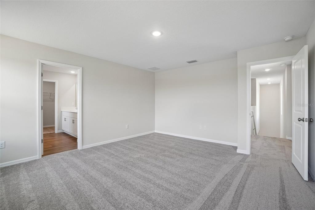 A carpeted bedroom features two doorways, one leading to a bathroom and another to a hallway — 36564 SAGEMOOR DRIVE, ZEPHYRHILLS, FL