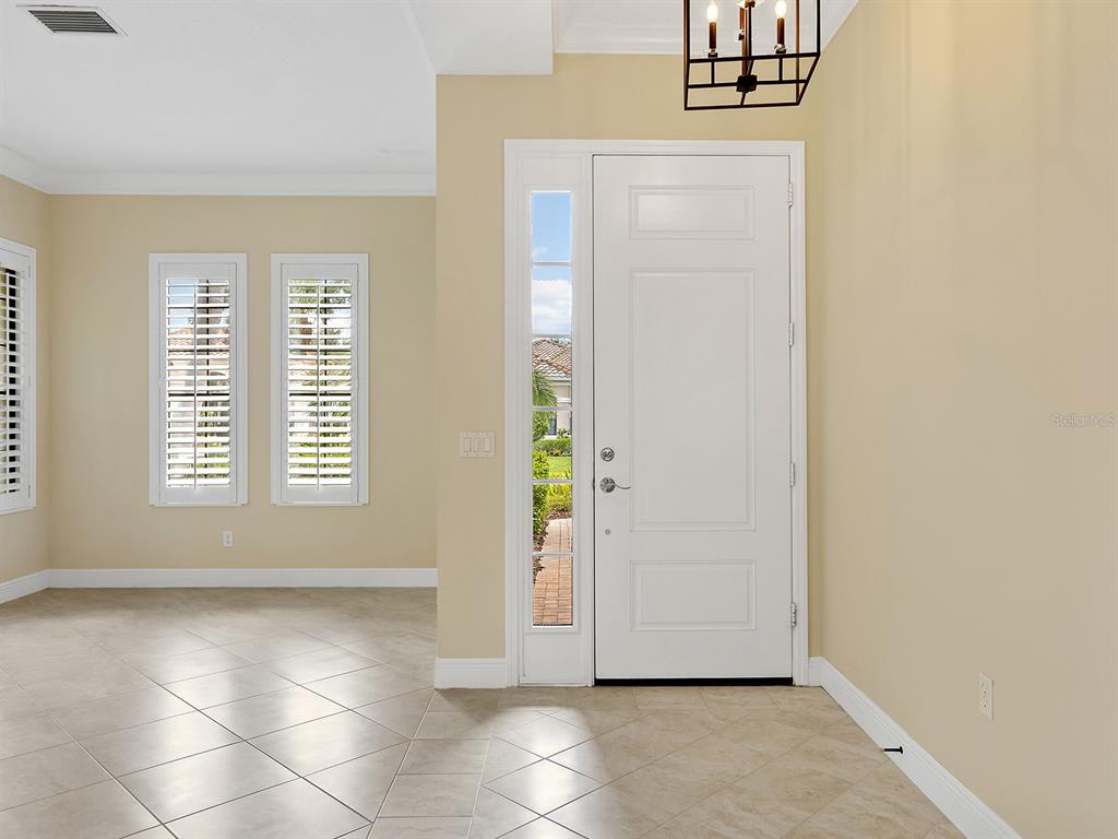 A bright entryway features beige walls, tile flooring, a white front door, and plantation shutters — 7210 LAKE FOREST GLEN, LAKEWOOD RANCH, FL