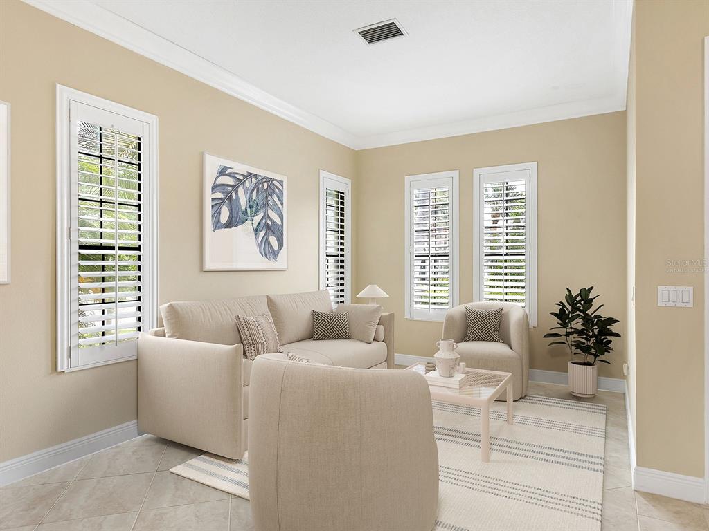 A living room with beige walls, tile flooring, plantation shutters, and neutral-toned furniture — 7210 LAKE FOREST GLEN, LAKEWOOD RANCH, FL