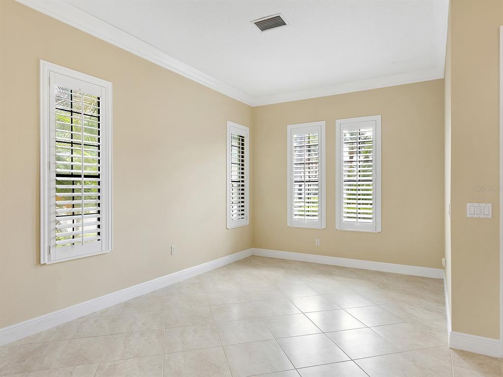 An empty room with beige walls, tile flooring, and white plantation shutters on the windows — 7210 LAKE FOREST GLEN, LAKEWOOD RANCH, FL