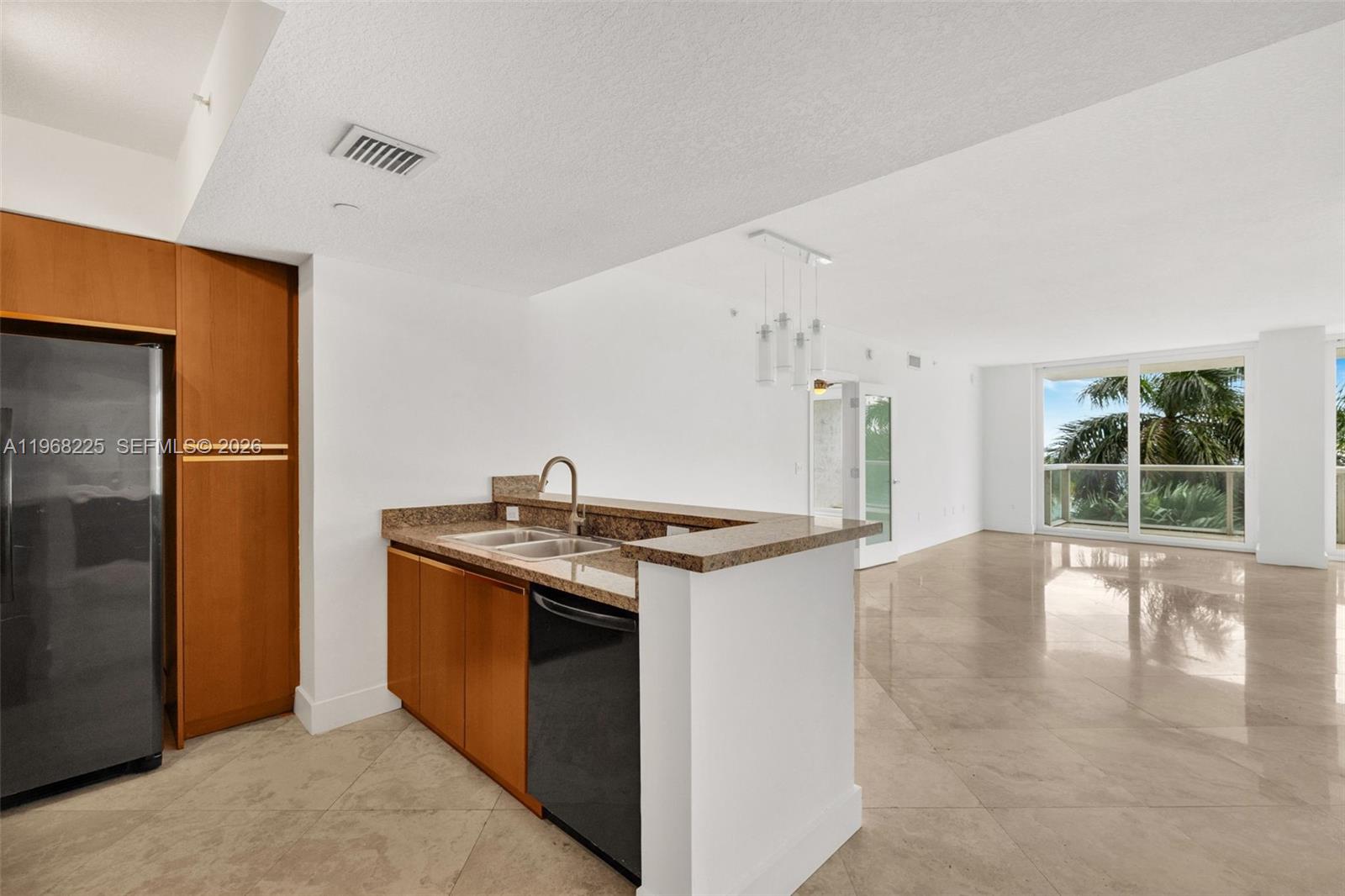 A kitchen with wood cabinets and granite countertops opens into a bright living area — 10 Venetian Way # 403, Miami Beach FL 33139, MIAMI BEACH, FL