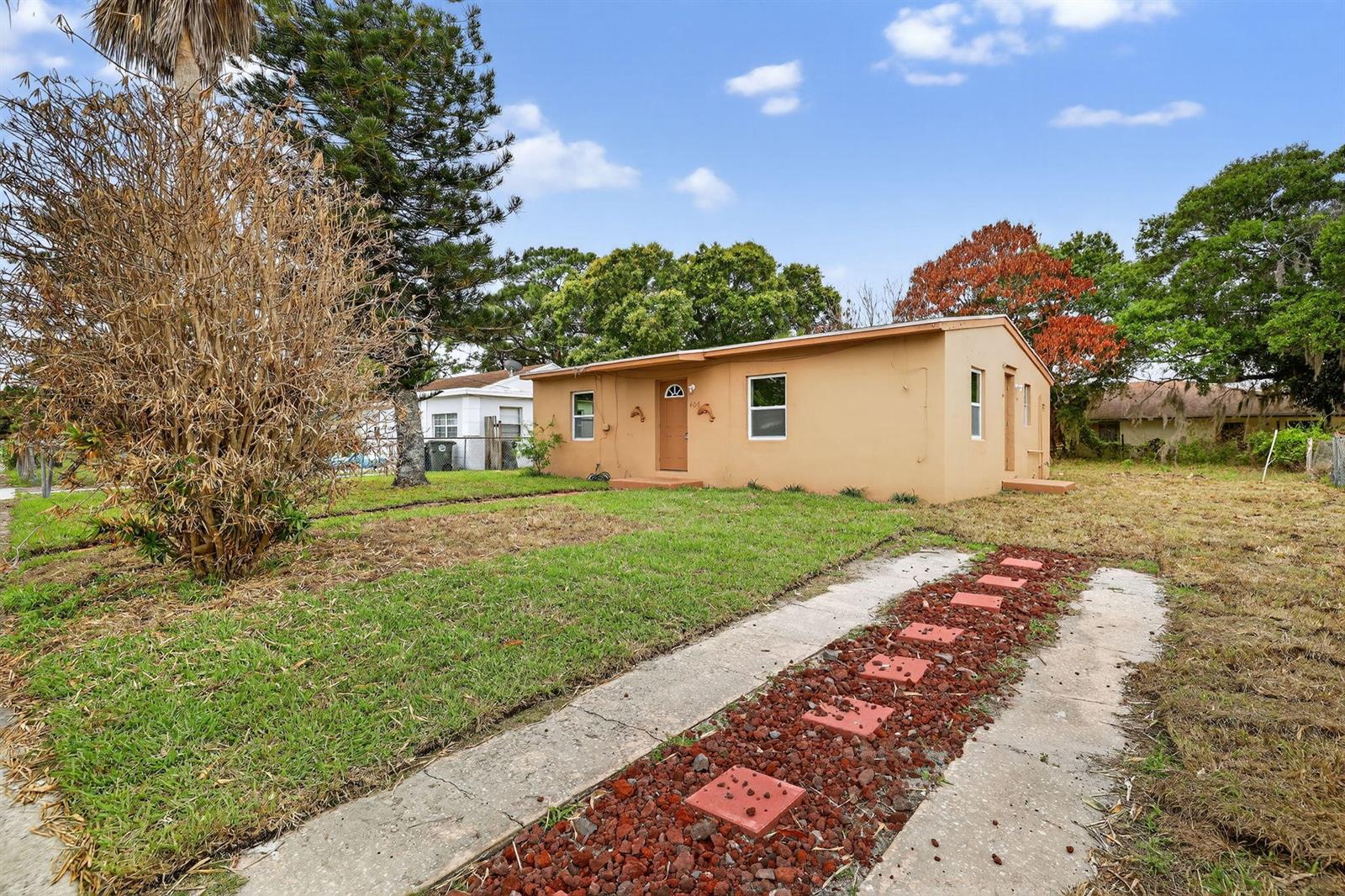 A single-story tan house with a concrete driveway and a front yard with trees — 405 N 22nd Street, Fort Pierce FL 34950, FORT PIERCE, FL