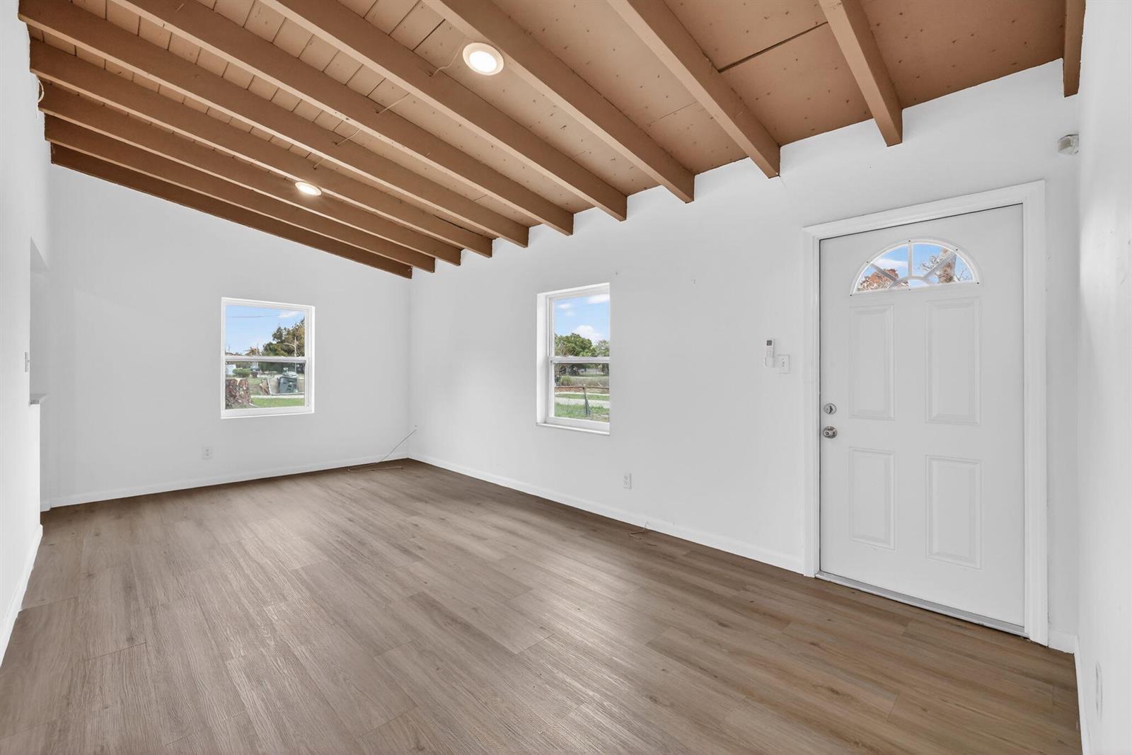 An empty room features white walls, wood-look flooring, and a vaulted ceiling with exposed beams — 405 N 22nd Street, Fort Pierce FL 34950, FORT PIERCE, FL