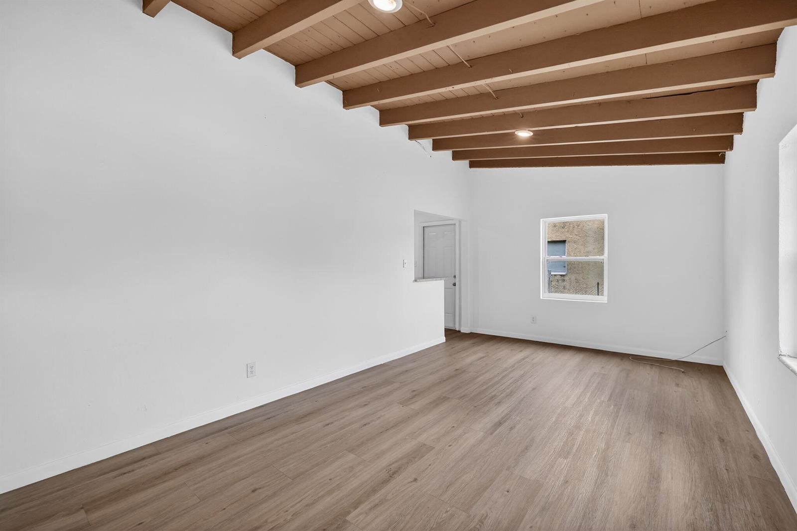 An empty room features white walls, wood-look flooring, and an exposed wood beam ceiling — 405 N 22nd Street, Fort Pierce FL 34950, FORT PIERCE, FL