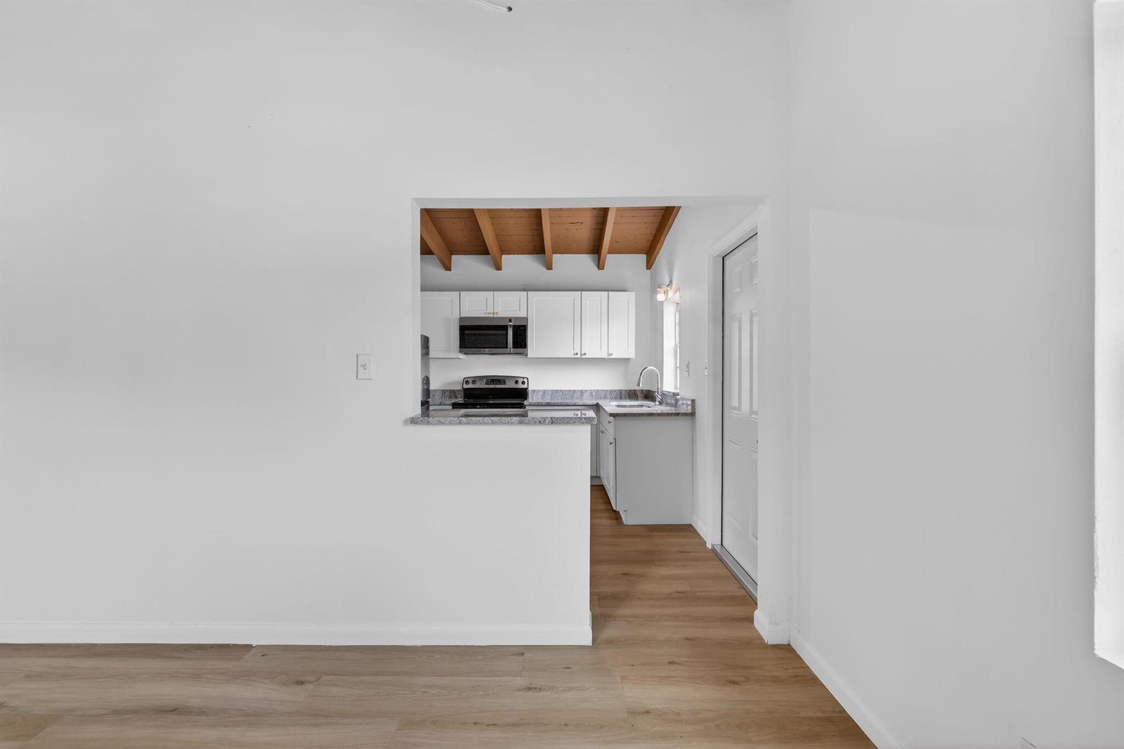 A view through a wall cutout into a kitchen with white cabinets and wood ceilings — 405 N 22nd Street, Fort Pierce FL 34950, FORT PIERCE, FL