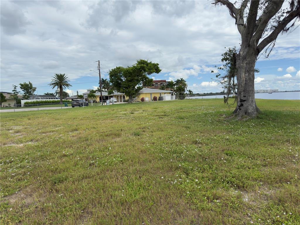 A large, grassy vacant lot overlooks a body of water with houses in the background — 266 BEENEY ROAD SE, PORT CHARLOTTE, FL