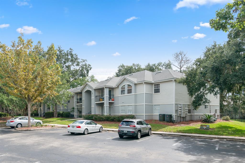 A multi-story apartment building with a parking lot in the foreground under a blue sky — 3705 SW 27TH STREET UNIT 1116, GAINESVILLE, FL