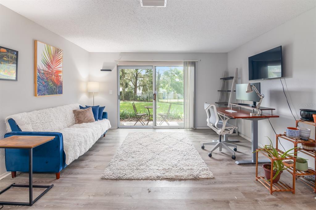 A living room features a blue sofa, a desk, a white rug, and sliding glass doors — 3705 SW 27TH STREET UNIT 1116, GAINESVILLE, FL