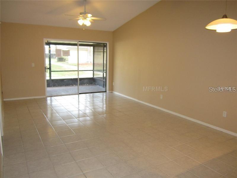 A living room with light-colored tile flooring, a ceiling fan, and sliding glass doors — 13 SILVER PARK CIRCLE, KISSIMMEE, FL