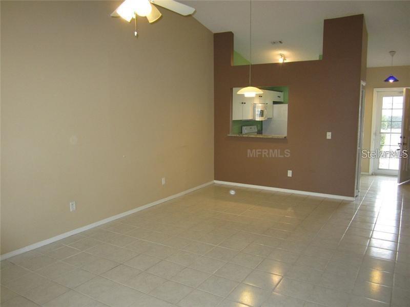 An open living area features light-colored tile flooring, beige walls, and a kitchen pass-through window — 13 SILVER PARK CIRCLE, KISSIMMEE, FL