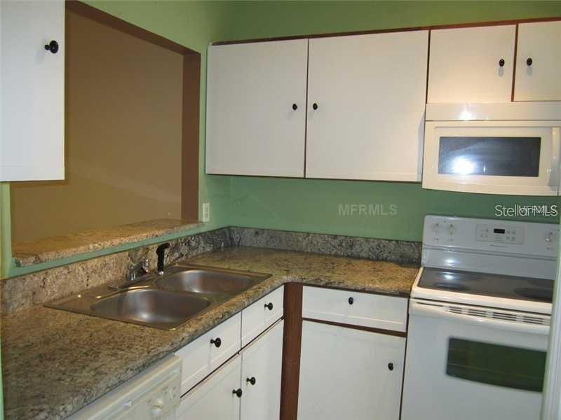 A kitchen features white cabinets, granite countertops, a double sink, and a white electric stove — 13 SILVER PARK CIRCLE, KISSIMMEE, FL