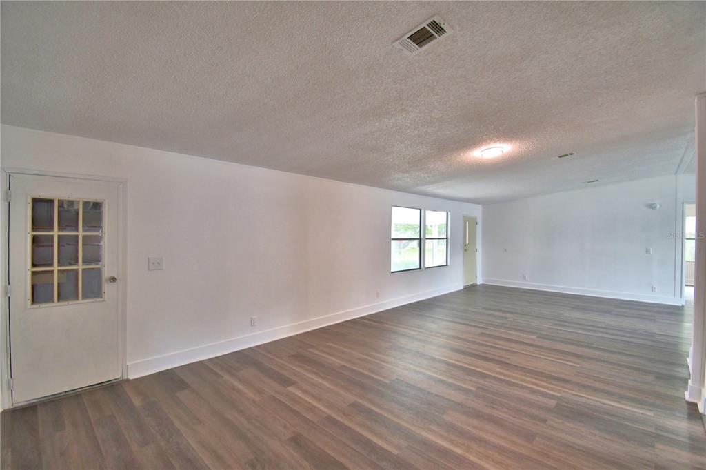 An empty living room with white walls, wood-look flooring, and a glass-paneled door — 306 TOWNBRIDGE DRIVE, HAINES CITY, FL