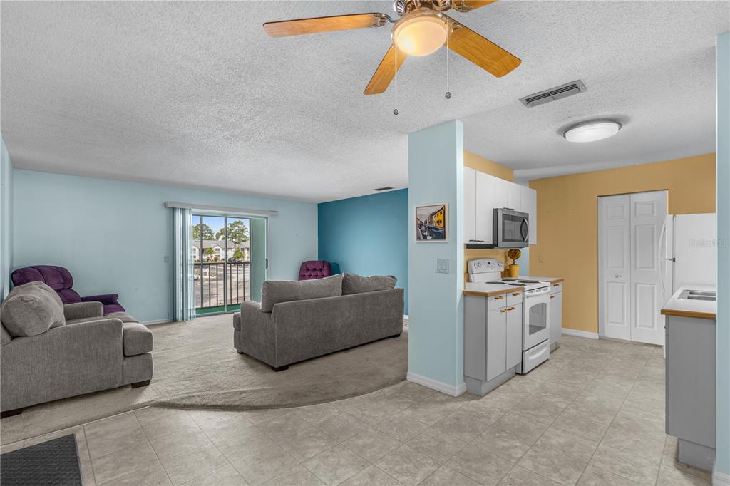 An open-concept living room and kitchen featuring carpeted and tiled floors and a ceiling fan — 101 BENT TREE DRIVE UNIT 13, DAYTONA BEACH, FL