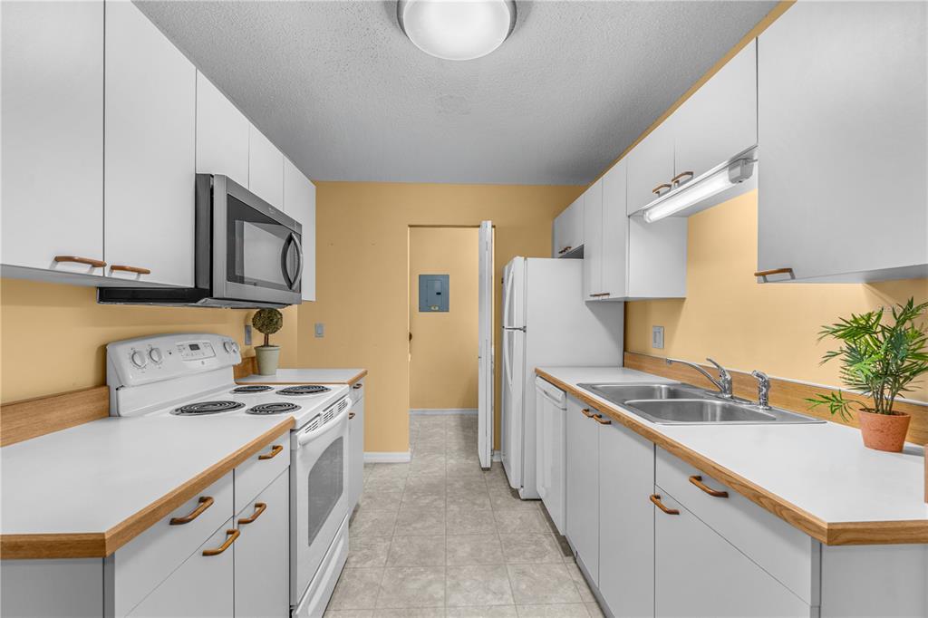 A galley kitchen features white cabinets, laminate countertops, a white stove, and a white refrigerator — 101 BENT TREE DRIVE UNIT 13, DAYTONA BEACH, FL