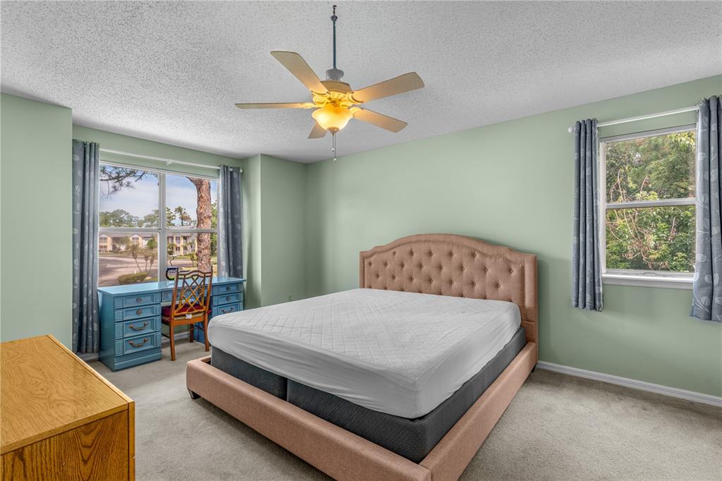 A bedroom with light green walls, a tufted bed, a ceiling fan, and a desk — 101 BENT TREE DRIVE UNIT 13, DAYTONA BEACH, FL