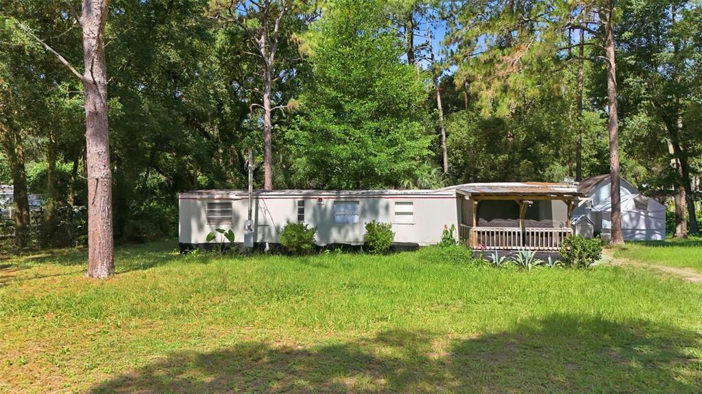 A single-story mobile home with a wooden porch sits on a grassy lot among trees — 43025 E 3RD STREET, PAISLEY, FL